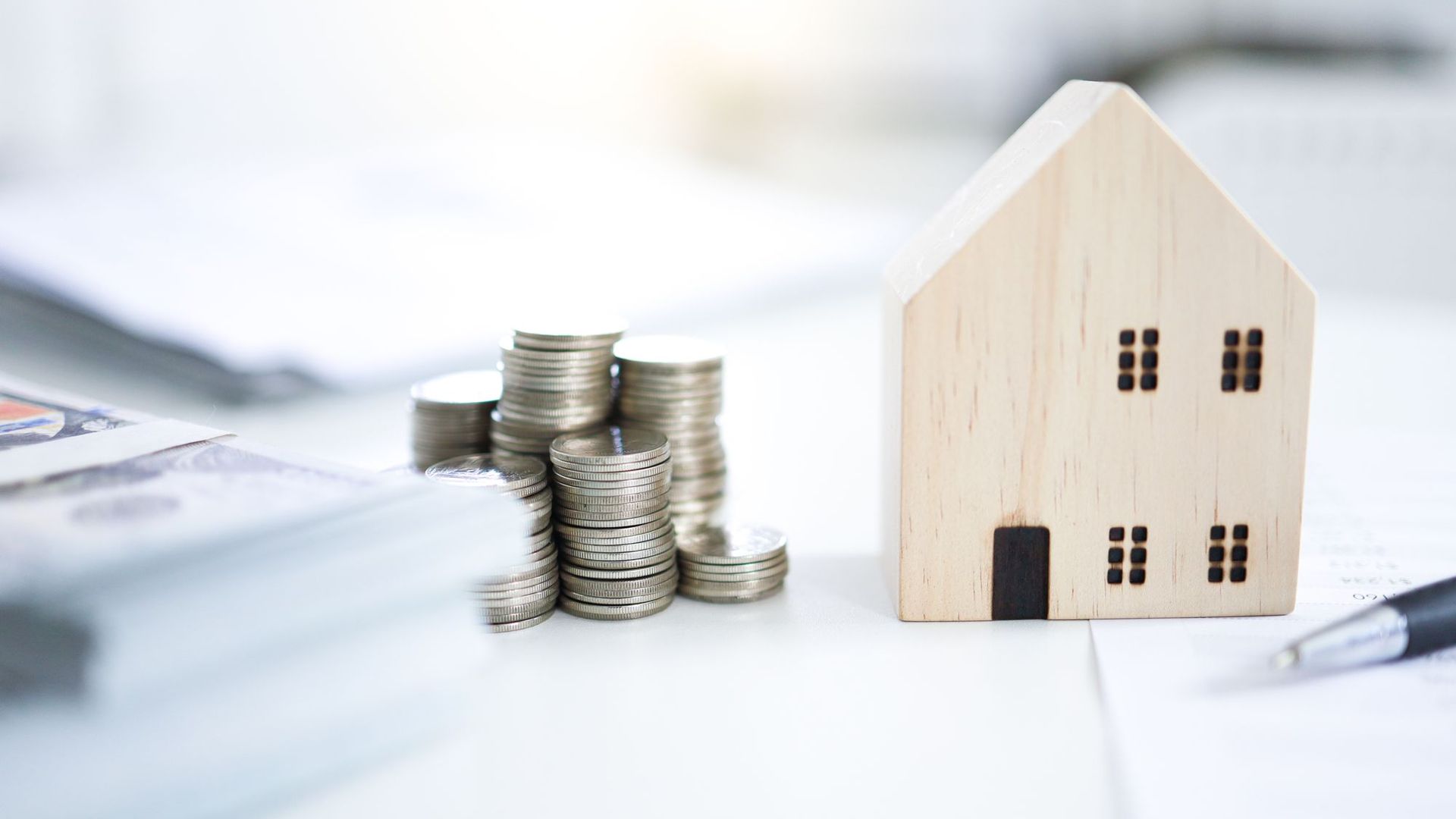 Münzstapel und Holzhaus auf einem Schreibtisch